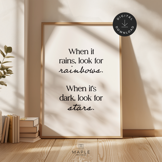 Motivational poster with quote 'when it rains, look for rainbows. when it's dark, look for stars' in modern black letters on a white background. Shown in a wood frame leaning on a wall.