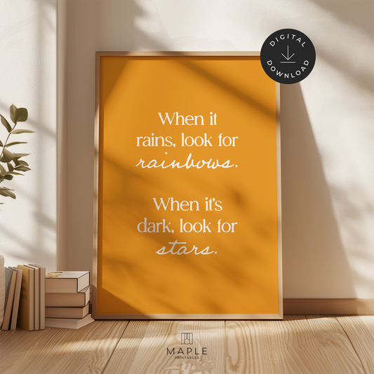 Colourful motivational poster with quote 'when it rains, look for rainbows. when it's dark, look for stars' in modern white letters on a dark yellow background. Shown in a wood frame leaning on a wall.